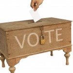 Hand dropping a ballot into a ballot box on www.adventuresinexpatland.com